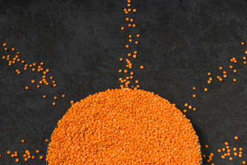Legumes on a dark background. Bright lentils in the shape of the sun with rays. Healthy food for vegans. Horizontal position. View up. Copy space