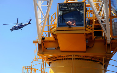 offshore helicopter passes over working crane
