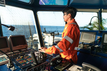 Filipino deck Officer on bridge of vessel or ship wearing coverall during navigaton watch at sea . He is maneuvering with cpp thrusters propulsion