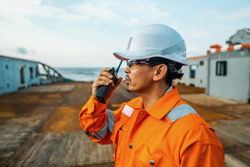 Filipino deck Officer on deck of vessel or ship , wearing PPE personal protective equipment. He holds VHF walkie-talkie radio in hands. Dream work at sea