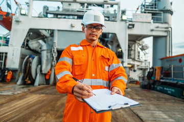 Filipino deck Officer on deck of offshore vessel or ship , wearing PPE personal protective equipment. He fills checklist. Paperwork at sea