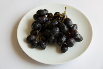 A bunch of juicy black grapes on awhite plate.