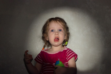 Fototapeta premium Little amazed, surprised girl with open mouth against the background of a rectangular frame of light from a movie projector on the wall.