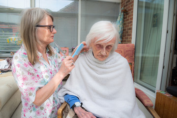 Obraz premium Elderly woman has hair cut by her carer during Corona virus lockdown at home.