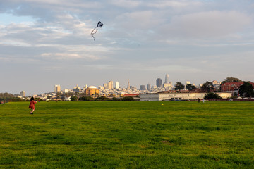 San Francisco skyline view from Crissy Field. Young women is playing with flying kite.