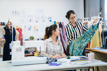 Two fashion designers women looking at piece of dress and checking mistakes. young girl coworkers discussing together with new season collection in workshop. group of female tailors working in studio