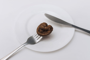 A fork strung artificial plastic feces of a cat which are lie on a white plate with knife close-up. The concept of an inept cook, a crappy restaurant, bad food, a taste of shit. Bad smelling joke.