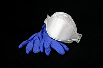 An N95 medical face mask and blue latex gloves for use to protect agains the spread of germs and COVID-19 virus, set against a plain black background.