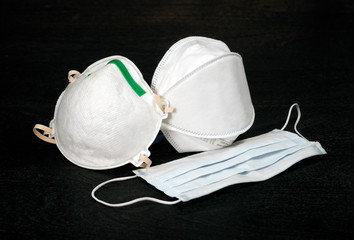 Three styles of N95 medical face masks for use to protect against contamination of respiratory infection, commonly used to protect agains the spread of COVID-19 virus, set against a black background.