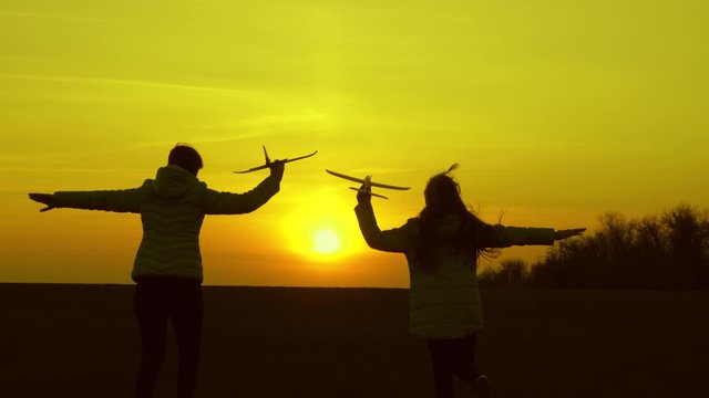free girls play with a toy airplane at sunset. Dreams of flying. healthy Children run in the sun with plane in hand. Happy childhood concept. Silhouette of children playing on plane