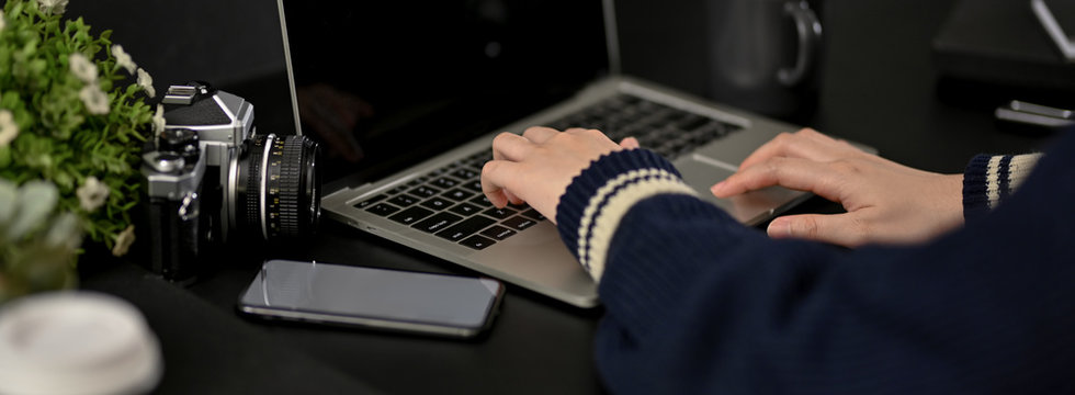 Cropped shot of female freelancer working with laptop on black table