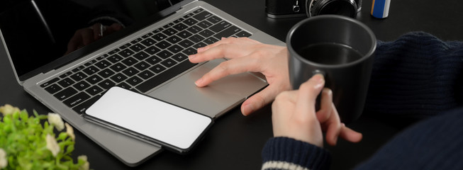 Cropped shot of businesswoman relaxing with hot coffee while working with laptop and mock-up smartphone