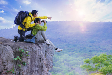 Couples hikers use binoculars to watching the view, sitting on top of the hill enjoy with nature