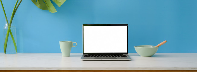 Close up view of creative workspace with blank screen laptop, breakfast meal and decoration on...