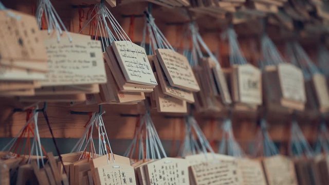 People and tourists visiting Kyakuden Meiji Shrine in Yoyogi park. Close up of message on wood label. Blurred temple in the background