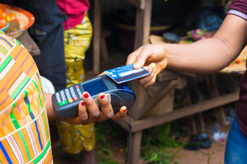 black lady shopping in a local market using credit card for payment. Young African trader holding a...