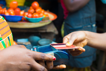 black lady shopping in a local market using credit card for payment. Young African trader holding a point of sale machine with a credit card. Woman making payment with Bank card