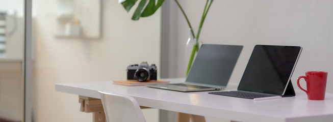 Cropped shot of comfortable office desk with laptop, digital tablet, mug, camera, office supplies and decoration
