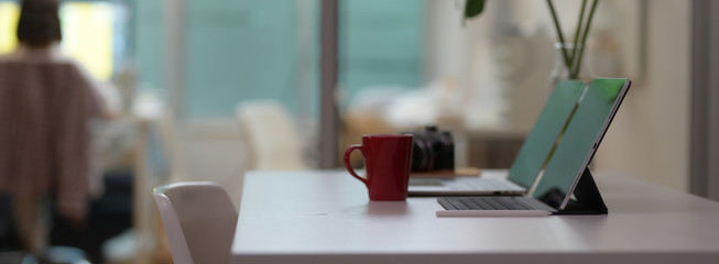 Side view of comfortable office desk with digital devices, coffee mug, camera and plant vase