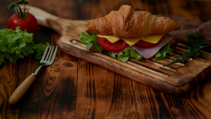 Close up view of breakfast meal with croissant sandwich ham and cheese on wooden tray