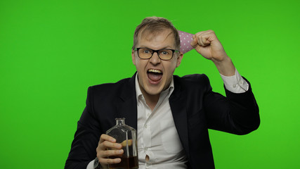 Drunk disheveled businessman in festive cap celebrates with alcohol bottle