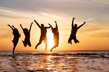 Five friends having fun and jumping at sunset beach