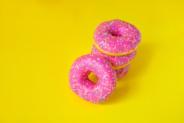 A stack of donuts with pink icing on a yellow background side view. Junk food. Sweets, pastries. Calories, fat.