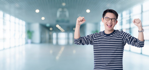 exciting smart casual asian male hand rise big toothy smile with blur office background successful asian male shout and cheerful gesture hand open ready to victory
