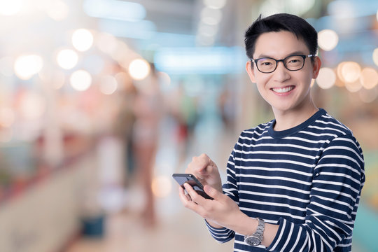 smart casual asian happiness male wear glasses smile and cheerful hand use smartphone ready to press buy button with shopping mall abstract blur background technology communication ideas concept