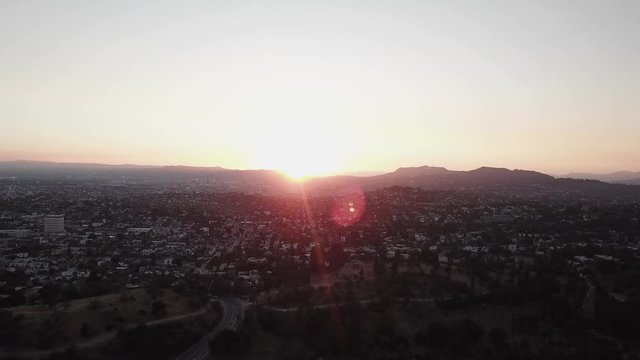 Wide aerial shot of urban sprawling city with sun peaking over mountain. 4K