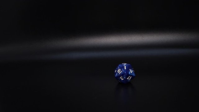 A blue die rolling into the off-center view landing so that a one is the number showing towards the camera.