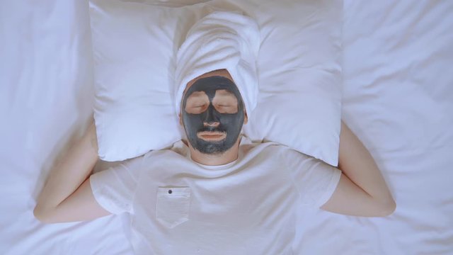 spa treatments top view adult caucasian man with black mudpack lies on bed looking at the camera happy smiling