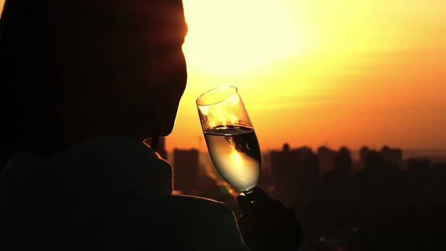 close up silhouette woman holding glass with wine looking on the urban cityscape sun up slow motion