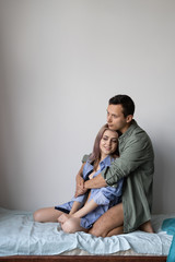 Loving young couple sitting at home on the bed. The guy hugs the girl. Lovers retired. Place for tex