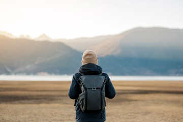 Hipster man traveler with sweater and backpack traveling at Napa Lake, Happy young Hiker looking mountain and sunset in trip Shangri-La,Yunnan,China. Explore, Adventure and Asia Solo travel concept