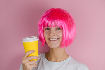 pretty happy young woman holding yellow  coffee to go cup against pink background