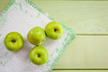 Ripe green apples on a green napkin lying on a canvas napkin and a wooden table surface. Background for fruits.
