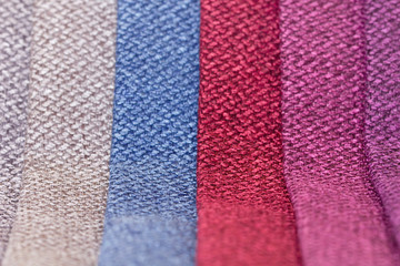 Samples of furniture upholstery in convolutions of red, blue, gray and purple. Background from rolls of multi-colored fabric close-up.