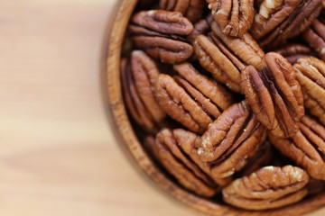 Pecan nuts close-up in a  round cup on a light wooden background.Healthy fats ingredient. Wholesome food and snack.Vegetarian and vegan food.