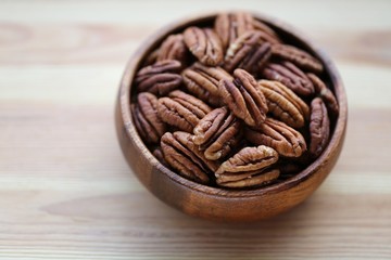 Pecan nuts close-up in a wooden round cup on a light wooden background.Healthy fats ingredient. Wholesome food and snack.Vegetarian and vegan food.