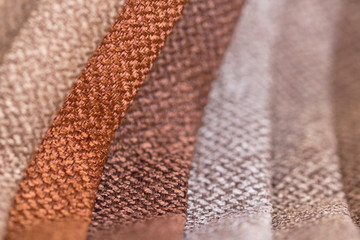 Samples of furniture upholstery in convolutions of orange, brown, beige and gray. Background from rolls of multi-colored fabric close-up.
