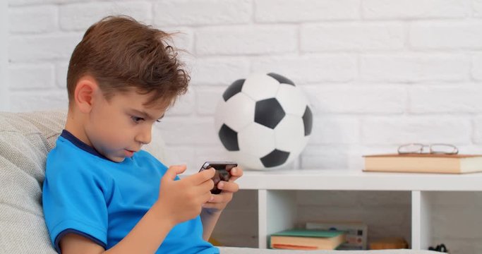 A six years old boy playing on mobile phone at home during quarantine COVID-19. Lifestyle in apartment. 4k