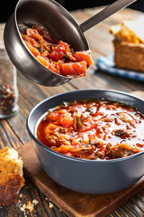 Borsch is poured into a bowl of soup ladle, traditional Ukrainian vegetable soup made from beets, carrots, tomatoes, potatoes, cabbage, herbs and garlic, close-up, shallow depth of field, selective