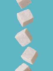 Tofu pieces in motion falling from above to down on blue background . Asian, vegan, protein, healthy food, falling and flying in the air.