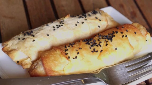 Fresh, hot pastry pies and black cumin on white plate with wooden background.