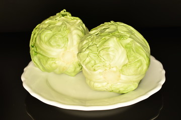 Fototapeta premium Green cabbage on a white ceramic plate, close-up, on a black background