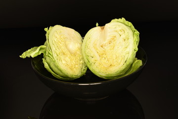 Two halves of a head of cabbage in a ceramic plate on a black background.