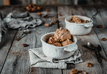 creamy caramel ice cream scoops with pecan nuts in white ceramic bowls on wooden table