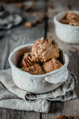 creamy caramel ice cream scoops with pecan nuts in white ceramic bowls on wooden table