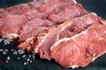 Fresh raw beef steaks on a black slate plate . Raw rib eye steaks on a slate plate with salt and pepper. Steaks with spices  on black slate stone board.